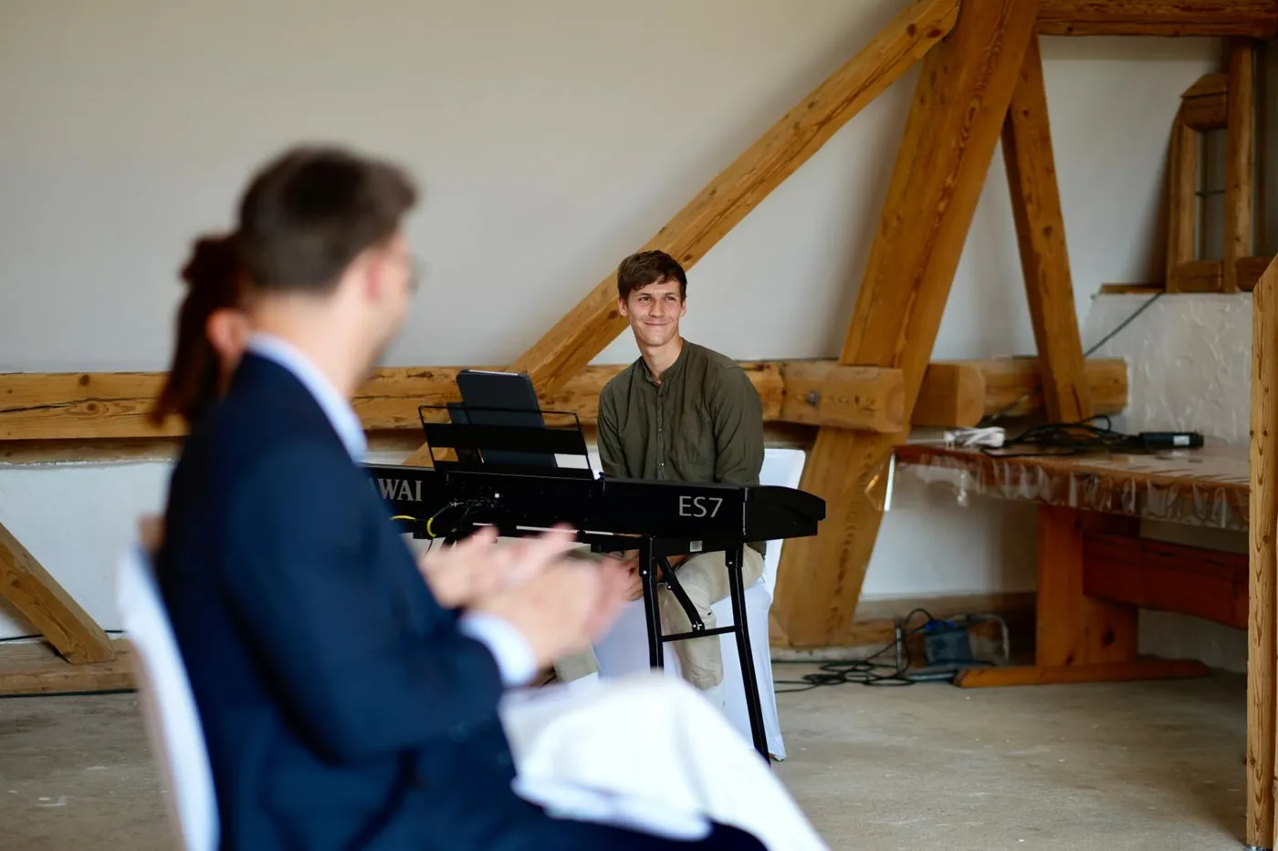 Silas am Klavier bei einer freien Trauung in einer Scheune mit Fachwerkbalken, im Vordergrund applaudierende Gäste